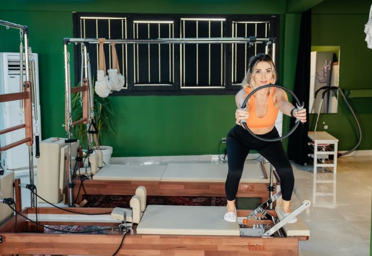 Fitness enthusiast practicing Pilates on a reformer machine in a modern, brightly lit studio.