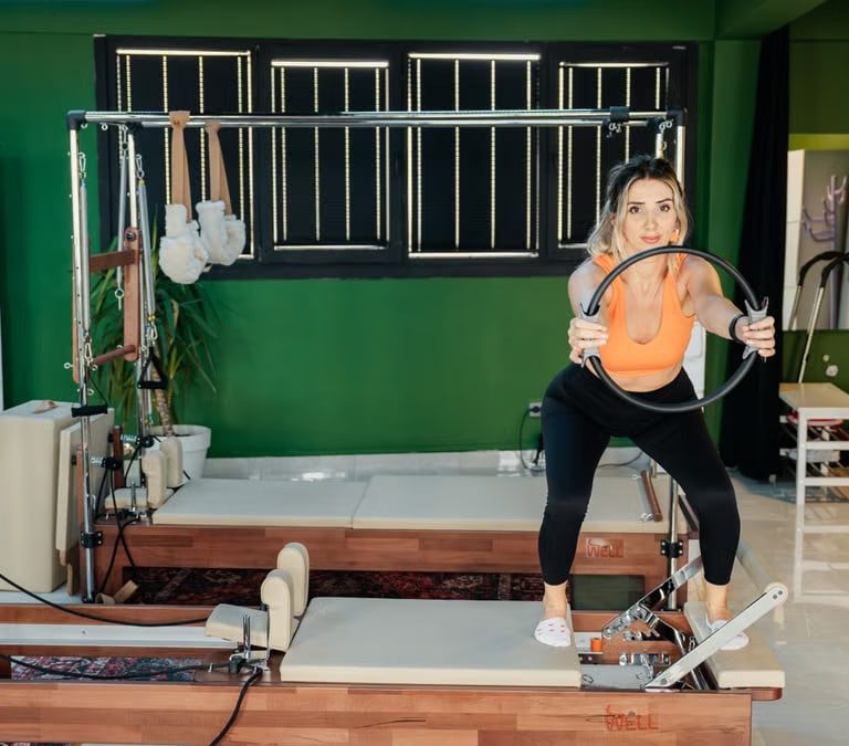 Fitness enthusiast practicing Pilates on a reformer machine in a modern, brightly lit studio.